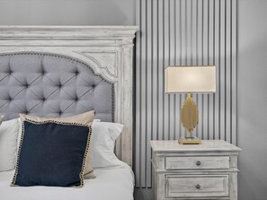 Quarto com cabeceira estofada, mesa de cabeceira com abajur e cômoda.