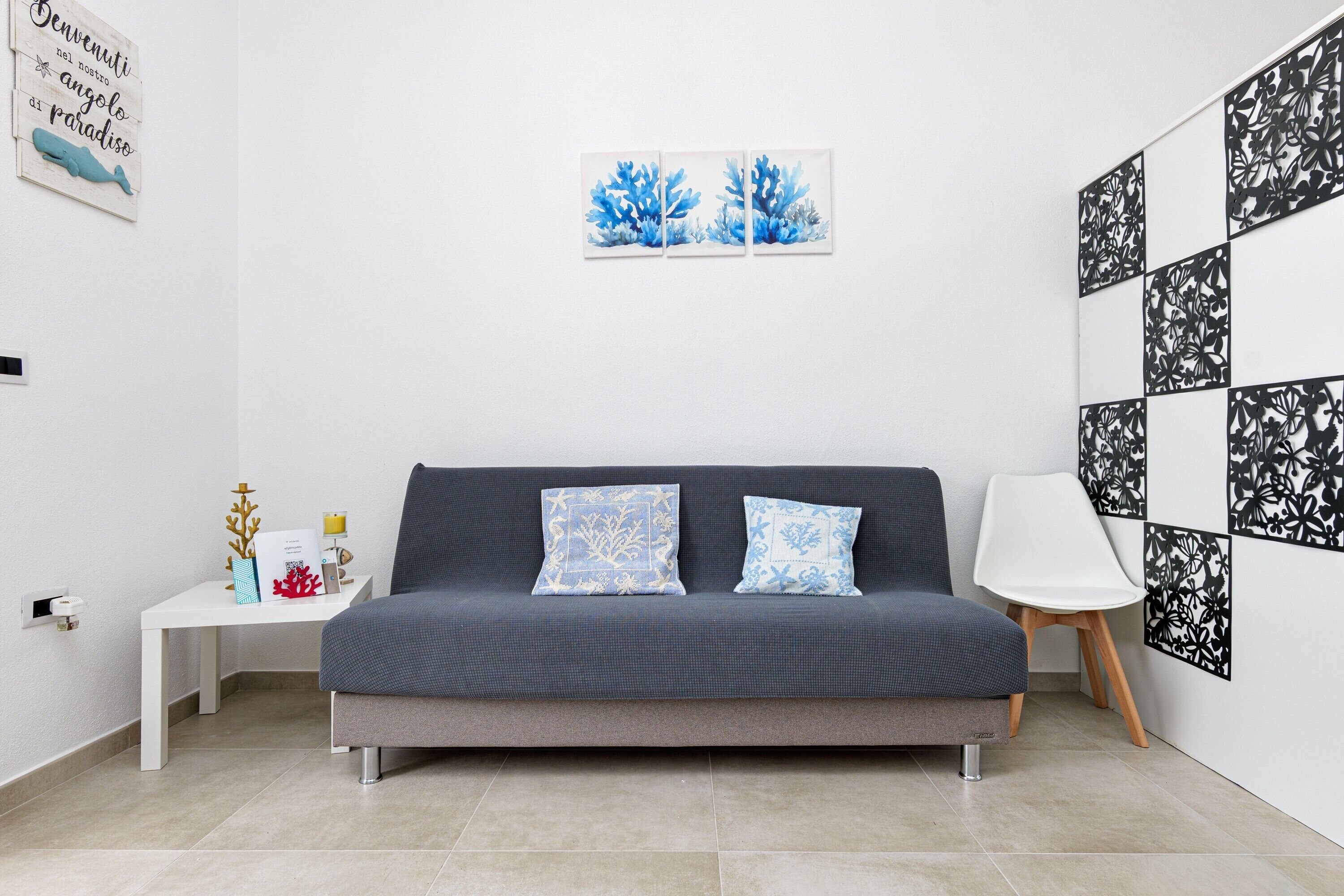 Un soggiorno moderno con un divano grigio, due cuscini decorati, un tavolino bianco con oggetti ornamentali e una parete con opere d'arte incorniciate.