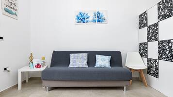 Un soggiorno moderno con un divano grigio, due cuscini decorati, un tavolino bianco con oggetti ornamentali e una parete con opere d'arte incorniciate.