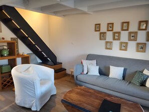 Un salon avec un canapé gris, un fauteuil blanc, une table basse en bois et un escalier.