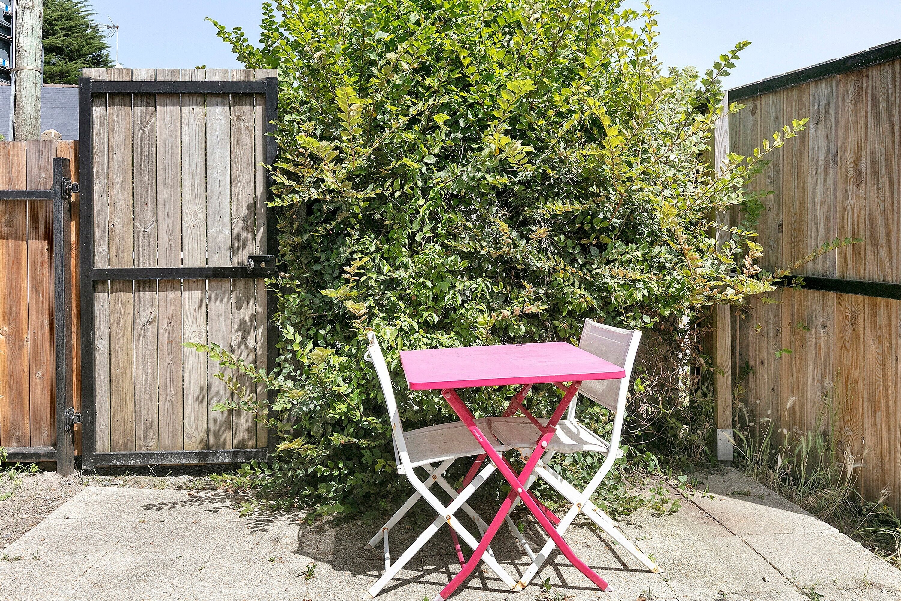 A wooden fence, a bush, and a white folding table with a pink top.