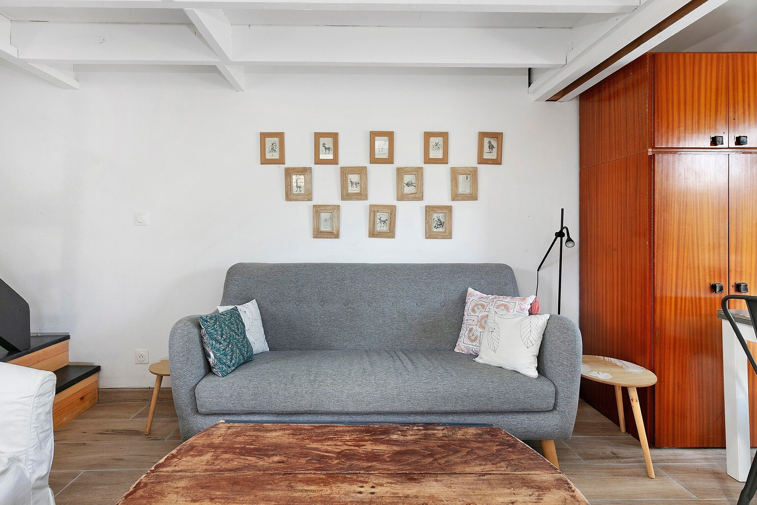 Una sala de estar con un sofá gris, un aparador de madera y cuadros en la pared.