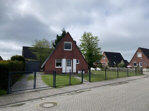 A row of red-brick houses with white doors and windows, a paved driveway, and a black metal fence.