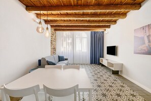 A modern living room with a wooden ceiling, a dining table with chairs, a sofa, a TV, and patterned flooring. - Ai Crocioni P3 Apartment with Wi-Fi and Air Conditioning (Verona)