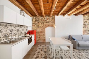 A kitchen with a stone wall, wooden beams, a white table, and a grey sofa. - Ai Crocioni P3 Apartment with Wi-Fi and Air Conditioning (Verona)
