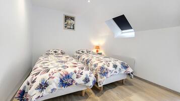 A bedroom with two beds, a skylight, a wall-mounted lamp, and a poster on the wall.