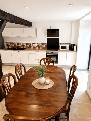 A modern kitchen with white cabinets, a wooden dining table, and a built-in oven. - Holiday Home 'Ker Marin - Maison Ty Gargouille' with Private Terrace, Garden & Wi-Fi (Sarzeau)
