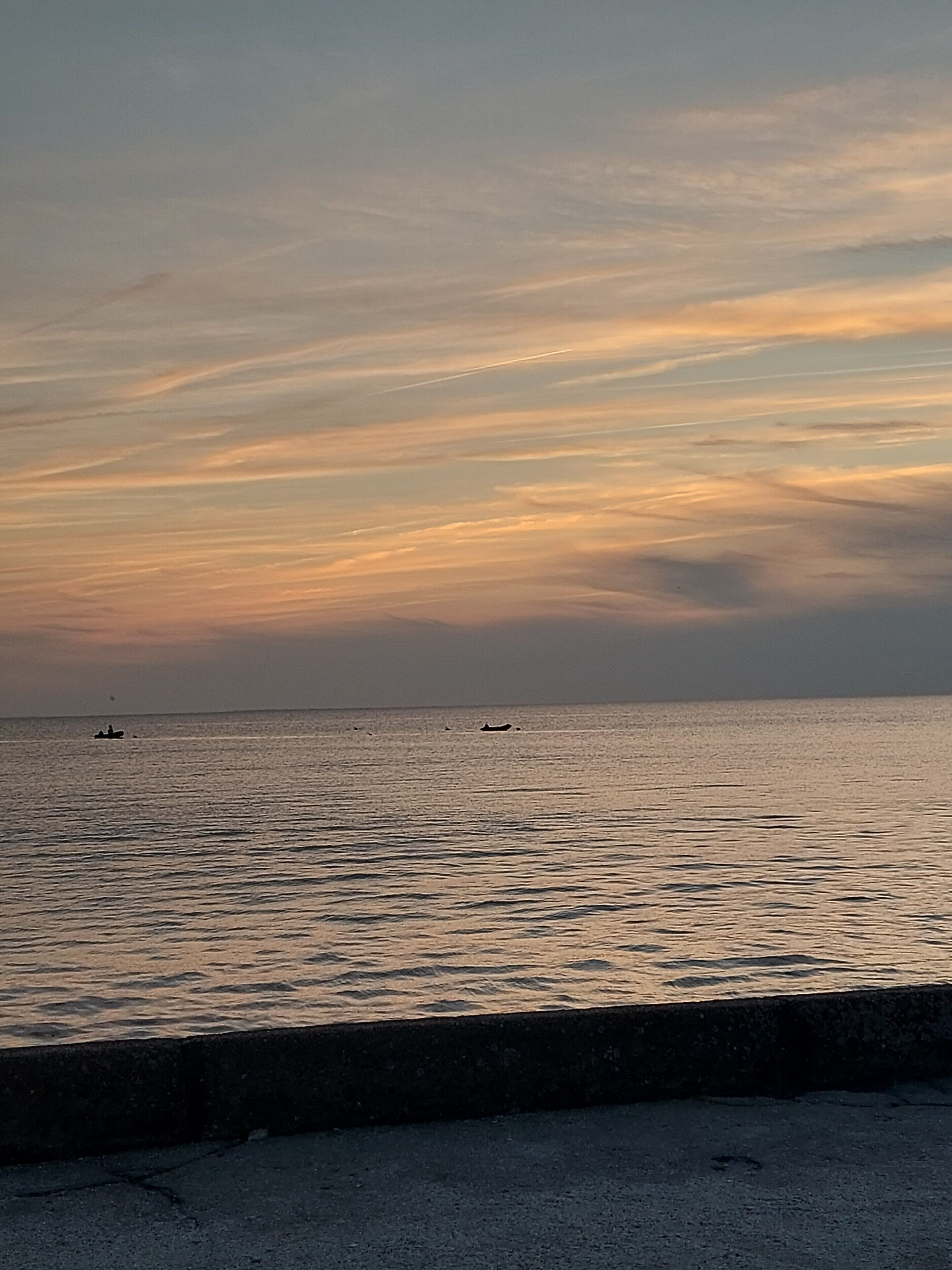 Een rustige zee met een heldere horizon en een betonnen barrière op de voorgrond.