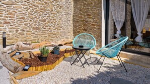 Un espace extérieur aménagé avec des murs en pierre, un bac à fleurs en bois planté, et deux chaises bleues.
