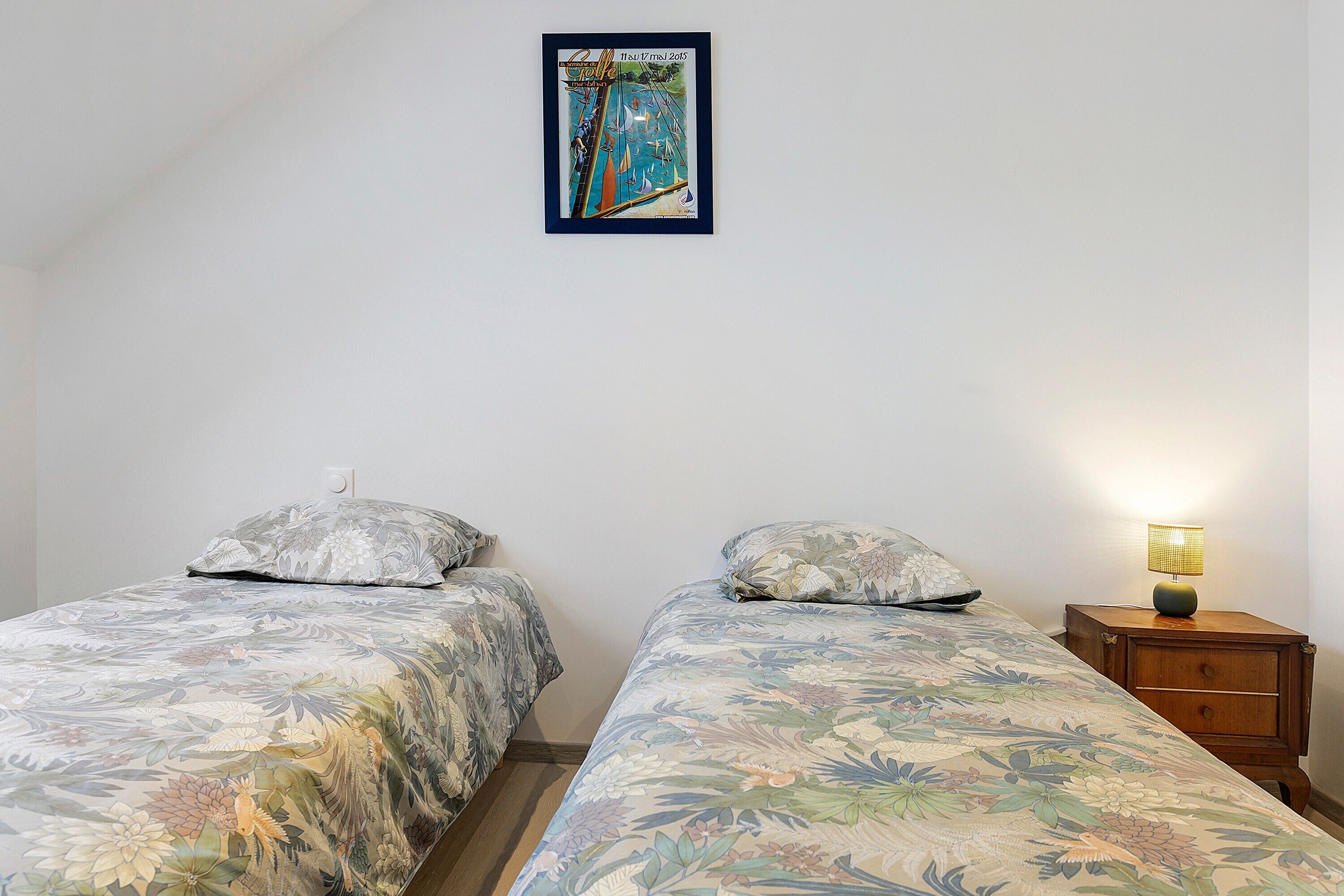 Un dormitorio con dos camas individuales, una mesita de noche con lámpara y un cuadro en la pared.