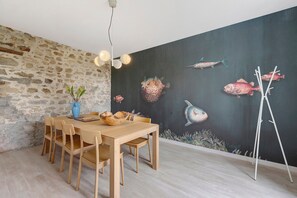 Ein Essbereich mit Holztisch und Stühlen, einer Steinwand und einem Wandgemälde von Fischen.