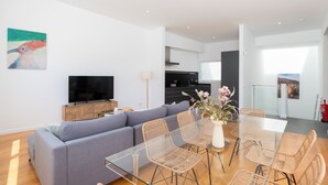 Ein modernes Wohnzimmer mit einer Couch, einem Glastisch, Korbstühlen, einem Flachbildfernseher und Kunstwerken an der Wand.