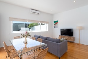 Una sala de estar moderna con una mesa de comedor de vidrio, un sofá gris y un televisor de pantalla plana.