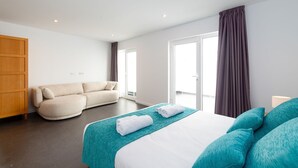 Ein Hotelzimmer mit einem Bett, einem Sofa, einem Holzschrank und einer Glastür, die auf einen Balkon führt.