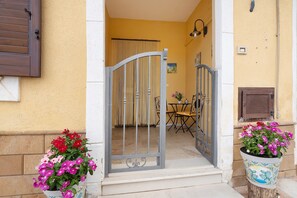 Une porte qui donne sur une pièce contenant une table et des chaises, une fenêtre avec des stores et un luminaire fixé au mur.