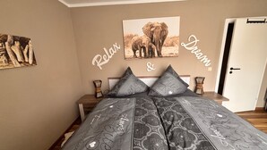 Ein Schlafzimmer mit einem Bett, einem Nachttisch, einem an der Wand hängenden Bild von Elefanten und einer Tür.