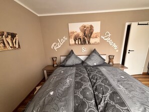 A bedroom with a bed, a nightstand, a wall-mounted picture of elephants, and a door.