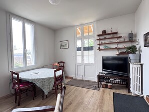 Une pièce comprenant une table à manger, des chaises, un téléviseur et des étagères remplies de divers objets.