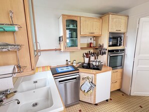 Una cocina compacta con armarios de madera, horno empotrado, lavavajillas y una pequeña encimera con hervidor.
