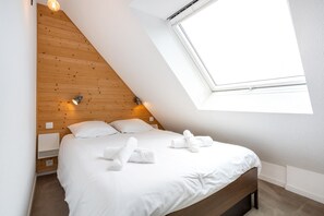 Ein Schlafzimmer mit schrägem Dach, einem Oberlicht, einem Bett mit weißer Bettwäsche und zwei Nachttischlampen.
