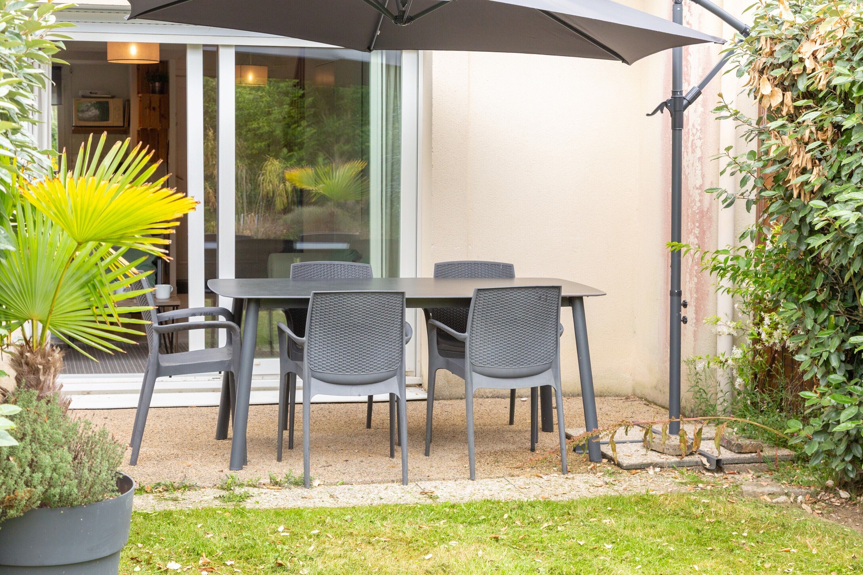 An outdoor patio with a table and chairs, a potted plant, and a sliding glass door leading to an interior space.