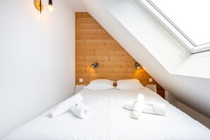 Ein Schlafzimmer mit schrägem Dach, einem hölzernen Kopfende, zwei Nachttischlampen und einem Oberlicht.