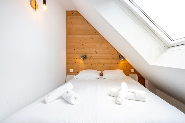 A bedroom with a sloped ceiling, a wooden headboard, two bedside lamps, and a skylight.
