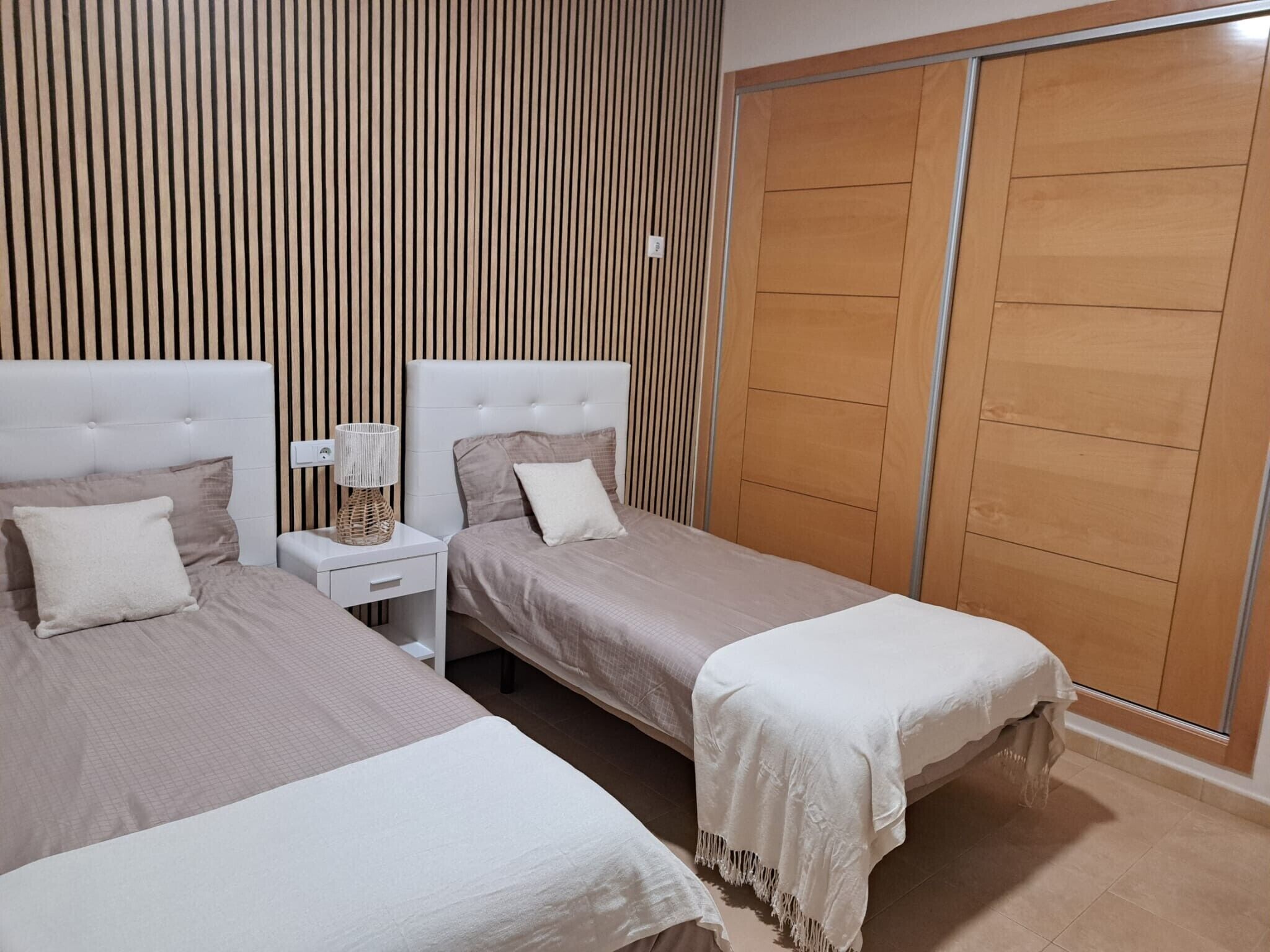 Une chambre avec deux lits, une table de chevet, une lampe et une armoire.
