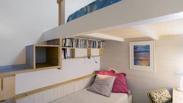Un dormitorio con literas, una estantería, una cama con almohadas, una silla y un cuadro en la pared.