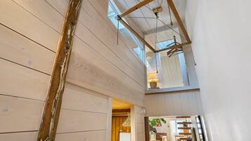 A wooden interior with a sloped ceiling, a hanging light fixture, and a view through a window.