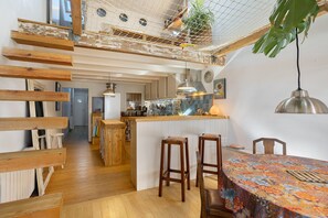 A modern kitchen with wooden beams, a hanging net, and a dining area with a colorful tablecloth. - “At the Foot of the Market” La Rochelle, City Center (La Rochelle)