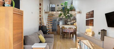Uma sala de estar aconchegante com um sofá cinza, um armário de madeira e um espaço de refeições com mesa e cadeiras.