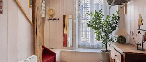 A cozy room with a wooden staircase, a red bench, a potted plant, and a window with a decorative screen.