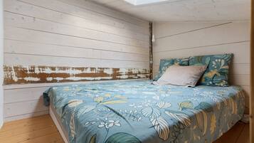 A bedroom with a sloped ceiling, a bed with floral bedding, a headboard with distressed paint, and a skylight.