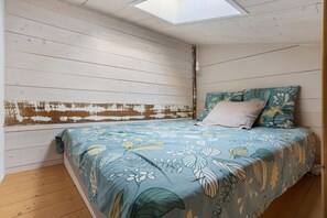 A bedroom with a sloped ceiling, a bed with floral bedding, a headboard with distressed paint, and a skylight. - “At the Foot of the Market” La Rochelle, City Center (La Rochelle)
