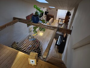 Une pièce de style loft avec un plancher en bois, un hamac, un pot bleu contenant une plante et un piano.