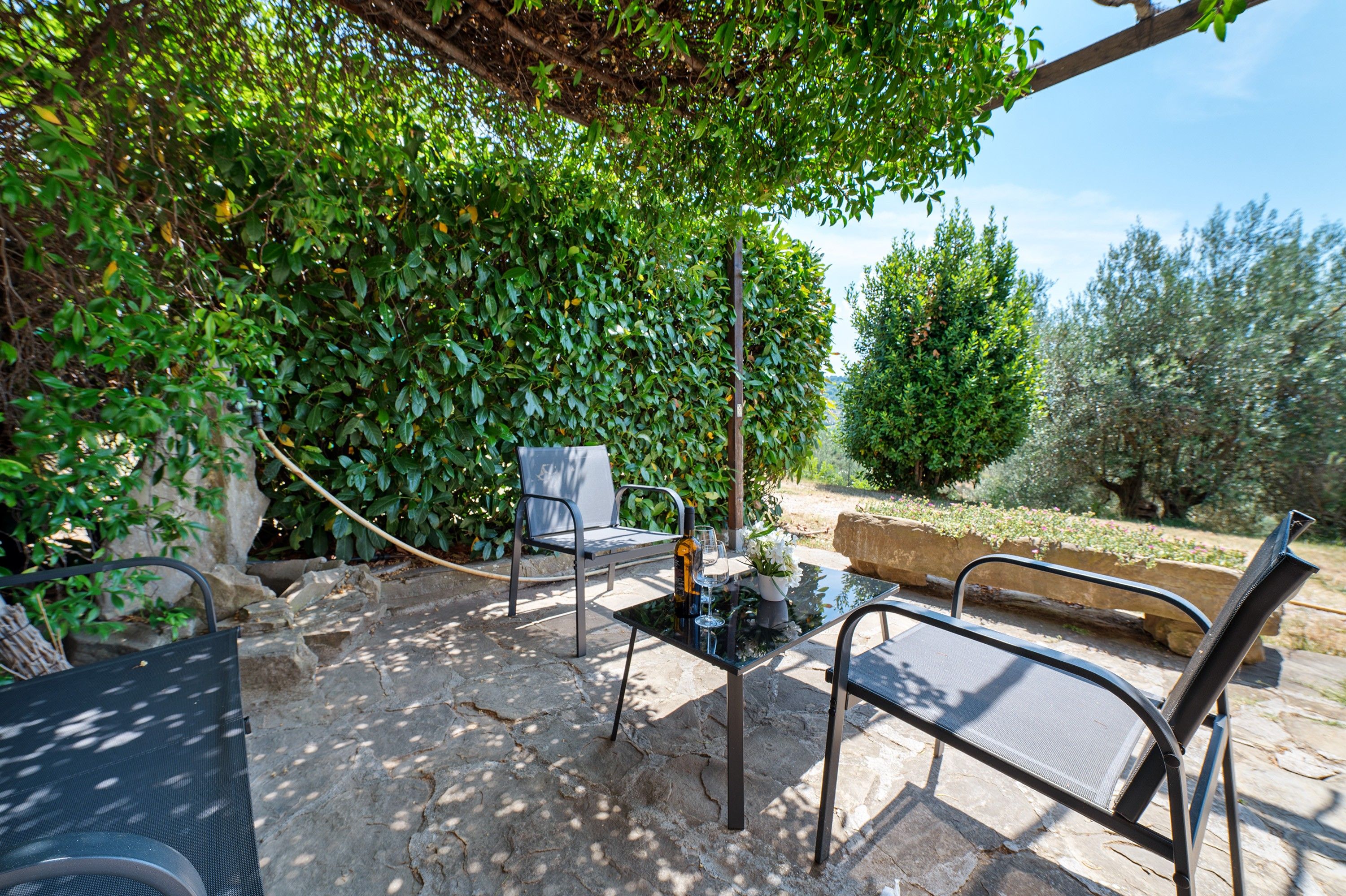 An outdoor patio with two metal chairs, a glass table, and a bottle.