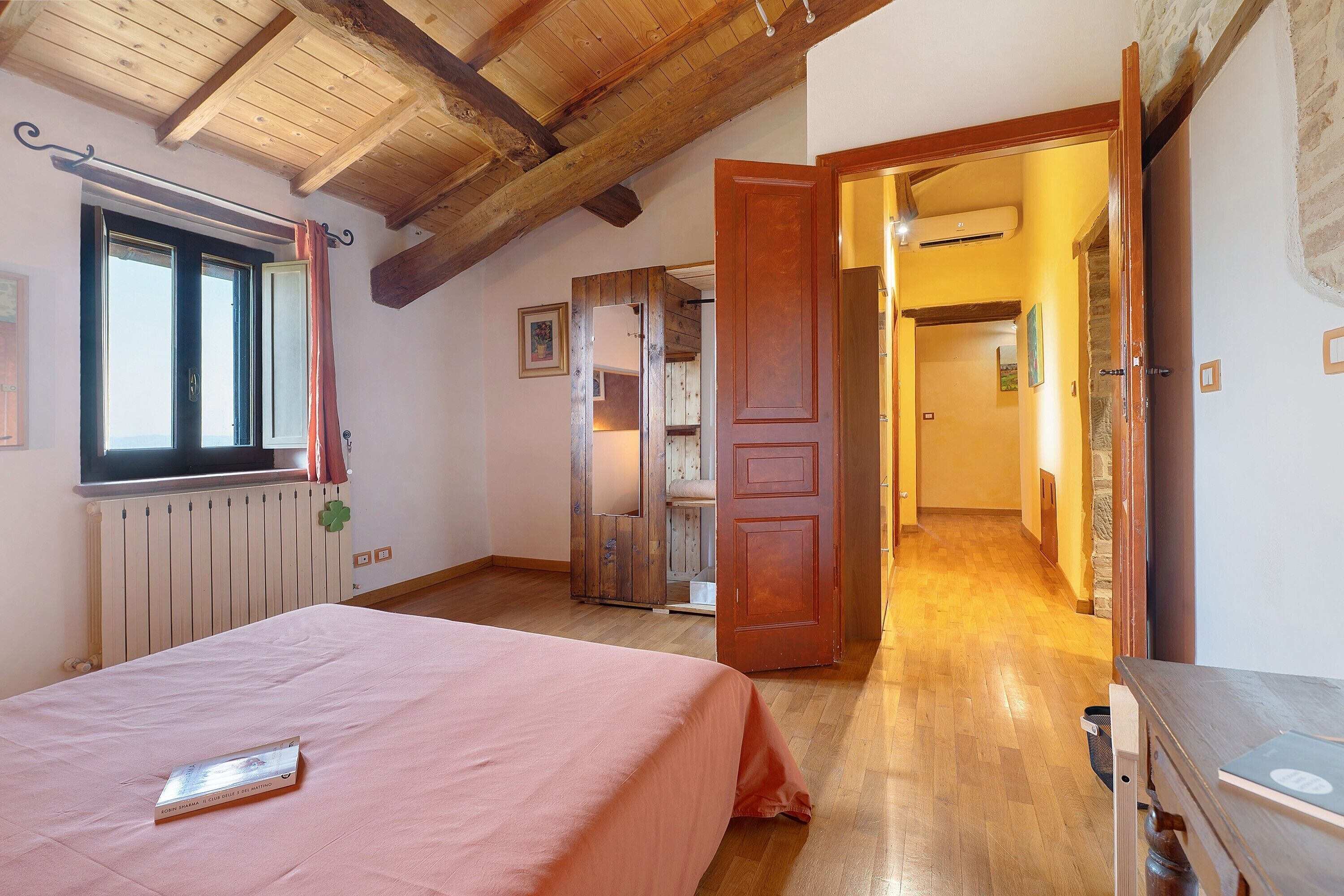 A bedroom with a bed, a window, a radiator, and a wooden ceiling.