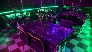 Una habitación con piso a cuadros, mesas con sillas y una cabina de DJ con iluminación verde.