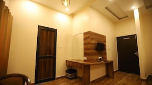 Una habitación con un escritorio de madera, un espejo, una puerta y un pequeño cubo de basura.