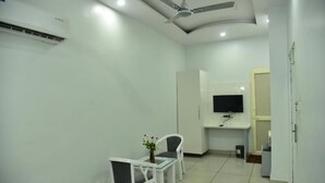 Una habitación limpia y moderna con ventilador de techo, televisor de pantalla plana montado en la pared, una pequeña mesa con sillas y un equipo de aire acondicionado blanco.