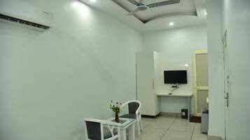 Una habitación limpia y moderna con ventilador de techo, televisor de pantalla plana montado en la pared, una pequeña mesa con sillas y un equipo de aire acondicionado blanco.