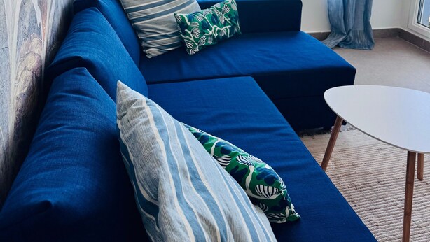 A room with a blue sofa, a small round table, and a view of the sea through large windows.