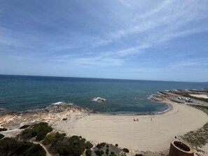 Una playa con arena, costa rocosa y cielo despejado.