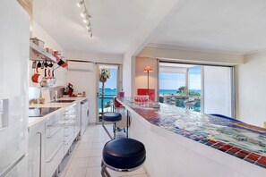 A modern kitchen with a tiled backsplash, a built-in oven, and a bar area with stools. - T3 Seafront Apartment with Sea View, Wi-Fi, and Air Conditioning (Cagnes-sur-Mer)