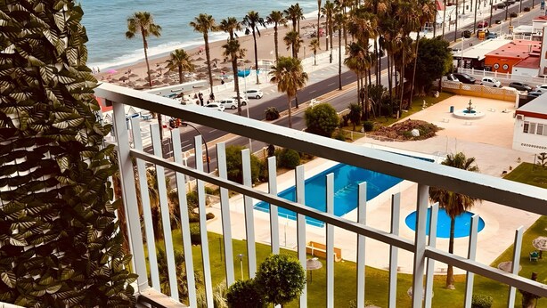 Ein Balkon mit Korbstühlen, einem kleinen Tisch mit einer Pflanze und Blick auf das Meer und den Strand.