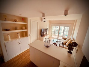 A compact living space with a kitchenette, a dining area with a glass table, a sofa, and a potted plant. - Apartment 'Olivanay' with Sea Views, Wi-Fi, and Air Conditioning (Benalmádena)