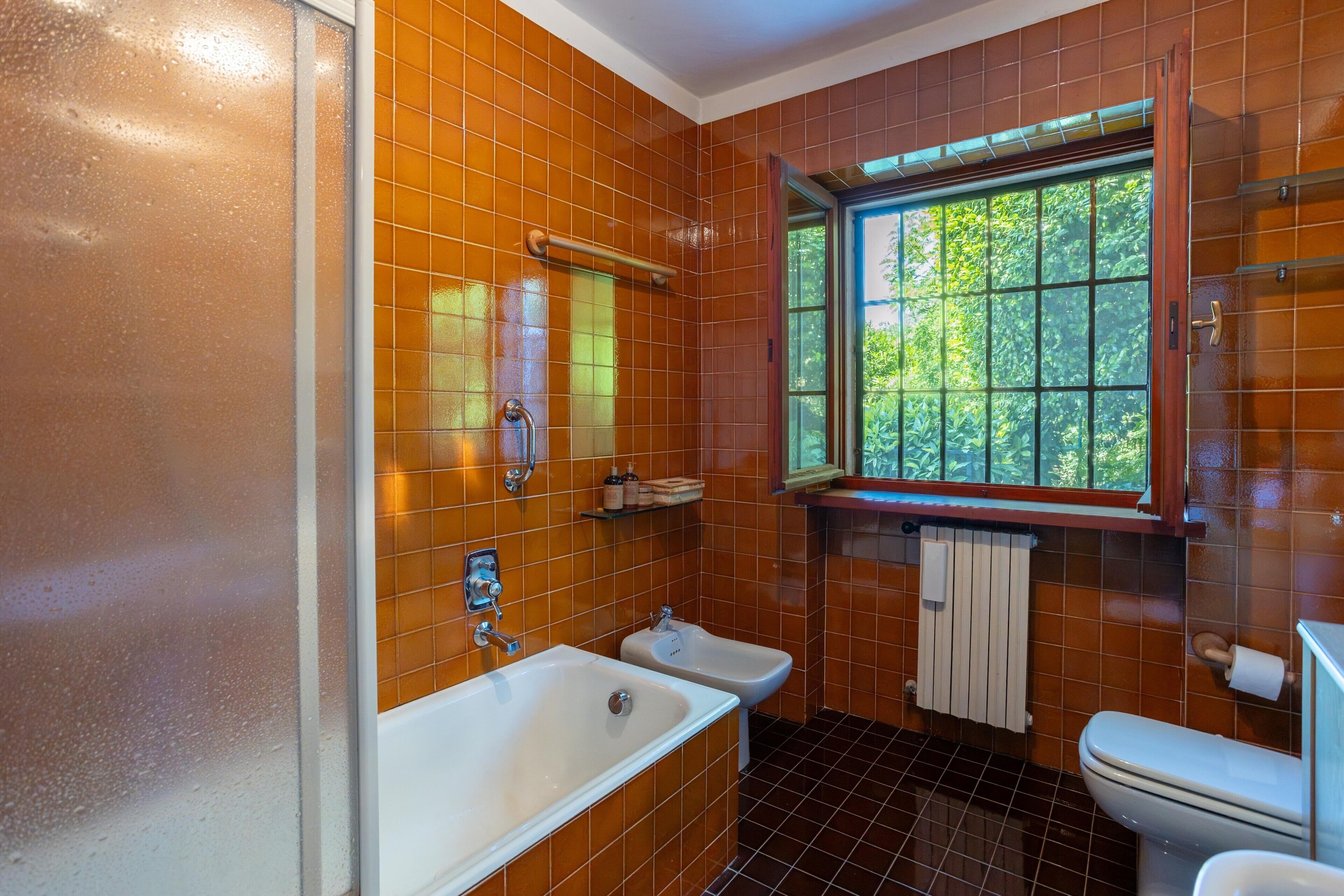 Un baño con bañera, un bidé, un inodoro y una ventana con vistas a zonas verdes.