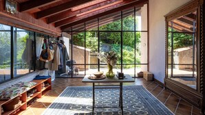 A spacious room with large windows, a wooden ceiling, a tiled floor, and a central table with a vase and bowl. - Groovy House: Vintage Charm, Lake Views, and Nature Retreat (Agra)