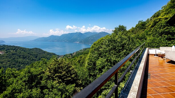 A terrace with a view of a lake and mountains, a railing, and a table with chairs. - Groovy House: Vintage Charm, Lake Views, and Nature Retreat (Agra)